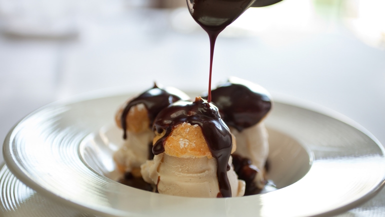 Drizzling chocolate sauce over profiteroles.
