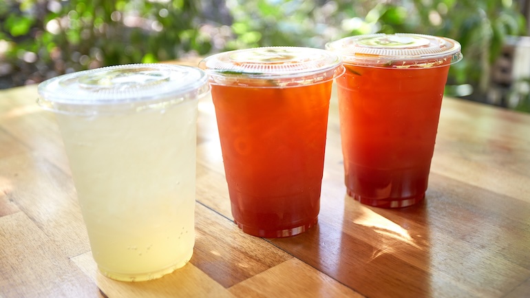 Three drinks in plastic cups with lids placed on a wooden table.