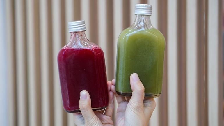 Hand holding two glass bottles of drinks for take away.