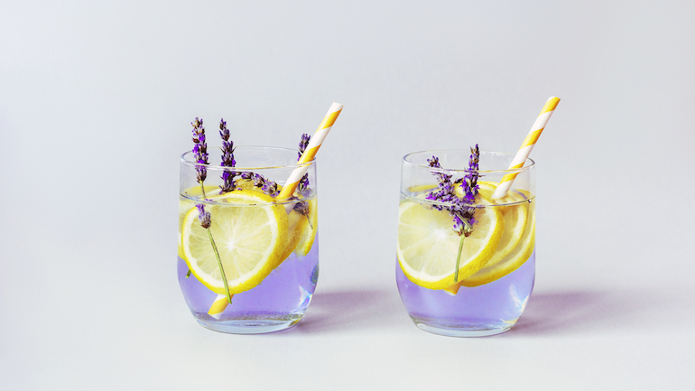 A close up of two glasses of lavendar lemonade with yellow straws.
